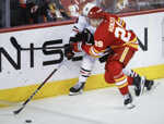 Slovenský hokejista v drese Calgary Flames Samuel Honzek (vpravo) a hráč Chicaga Blackhawks Jason Dickinson bojujú o puk